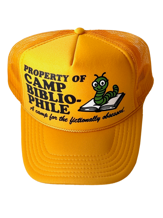 Photo of a gold yellow hat with "property of camp bibliophile, a camp for the fictionally obsessed" on it and a worm in a book